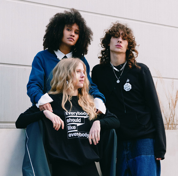 Three people outside, one wearing a black and white t-shirt reading “Everybody should like everybody”