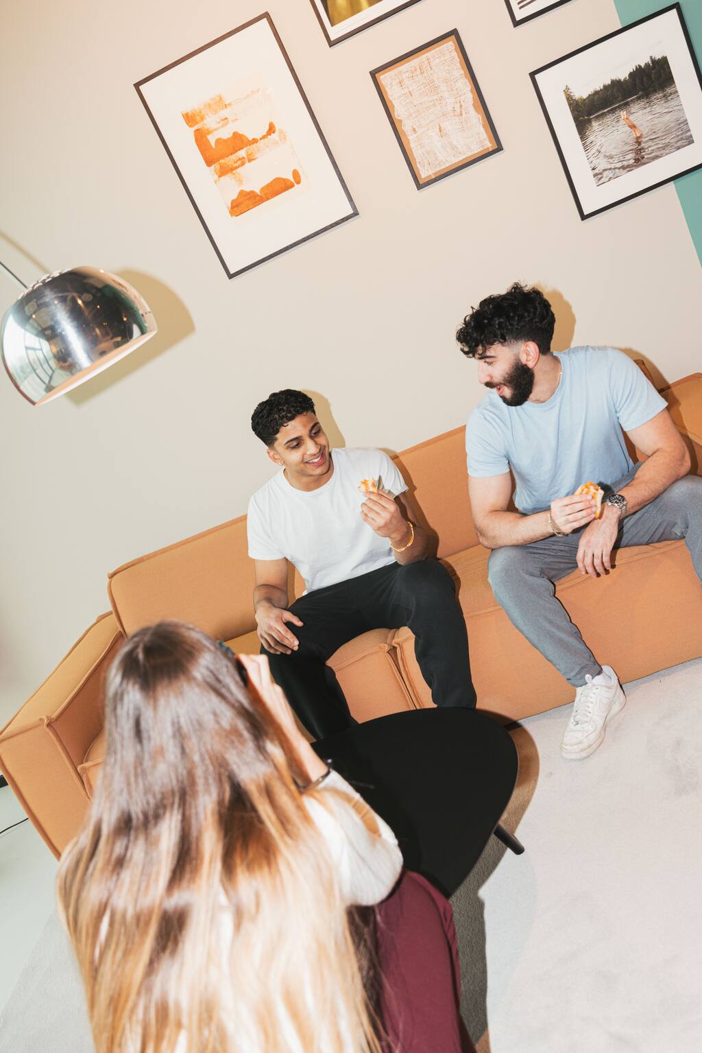 Friends sitting on orange sofa eating pizza and chatting indoors
