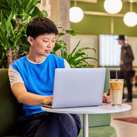 Woman working on laptop with iced coffee in modern coworking lounge