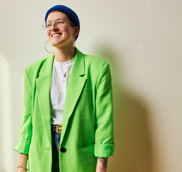 Jess Oberlin smiling and wearing a colorful outfit with green jacket and blue hat