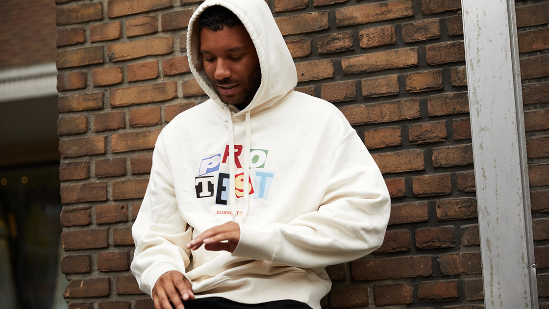 Gyor Moore against wall in Protest hoodie from Sobolt queer fashion brand