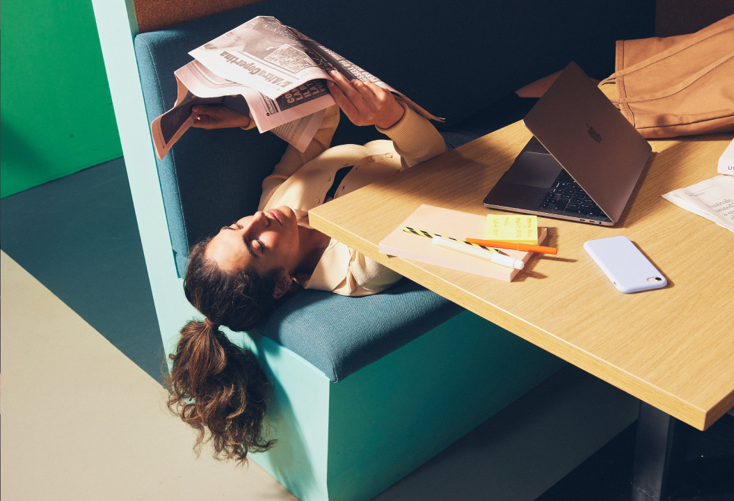 Girl reading a newspaper while laying on the bench at The Social Hub